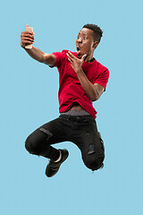 Image showing always on mobile. Full length of handsome young man taking phone while jumping