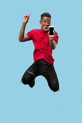 Image showing always on mobile. Full length of handsome young man taking phone while jumping