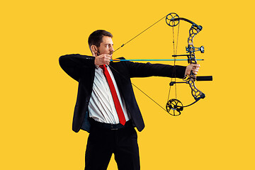 Image showing Businessman aiming at target with bow and arrow, isolated on yellow background