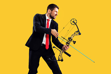 Image showing Businessman aiming at target with bow and arrow, isolated on yellow background