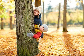 Image showing happy children peeking out tree at autumn park