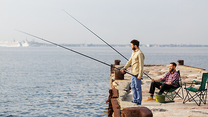 Image showing male friends with fishing rods on sea pier