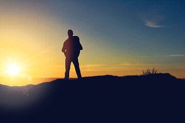 Image showing traveller standing on edge of hill over sunrise