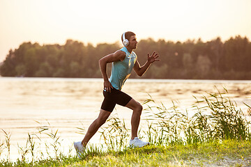 Image showing A young athletic man working out listening to the music at the riverside outdoors