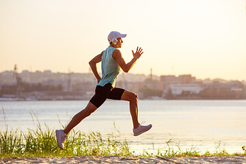 Image showing A young athletic man working out listening to the music at the riverside outdoors