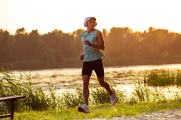 Image showing A young athletic man working out listening to the music at the riverside outdoors