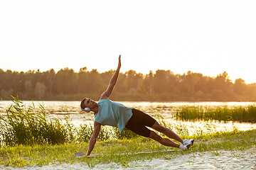 Image showing A young athletic man working out listening to the music at the riverside outdoors