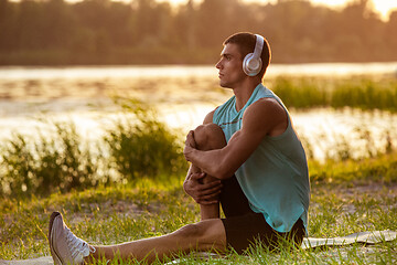 Image showing A young athletic man working out listening to the music at the riverside outdoors