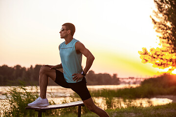 Image showing A young athletic man working out listening to the music at the riverside outdoors