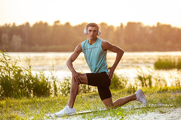 Image showing A young athletic man working out listening to the music at the riverside outdoors