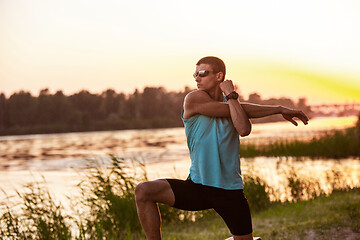 Image showing A young athletic man working out listening to the music at the riverside outdoors