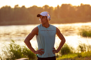 Image showing A young athletic man working out listening to the music at the riverside outdoors