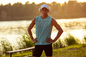 Image showing A young athletic man working out listening to the music at the riverside outdoors