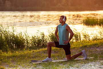 Image showing A young athletic man working out listening to the music at the riverside outdoors