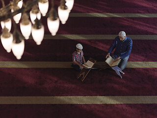 Image showing father and son in mosque praying and reading holly book quran to