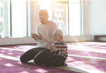 Image showing father and son in mosque praying and reading holly book quran to