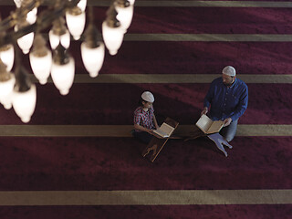 Image showing father and son in mosque praying and reading holly book quran to