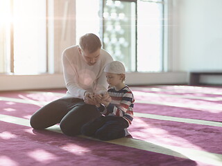 Image showing father and son in mosque praying and reading holly book quran to