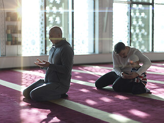 Image showing father and son in mosque praying and reading holly book quran to