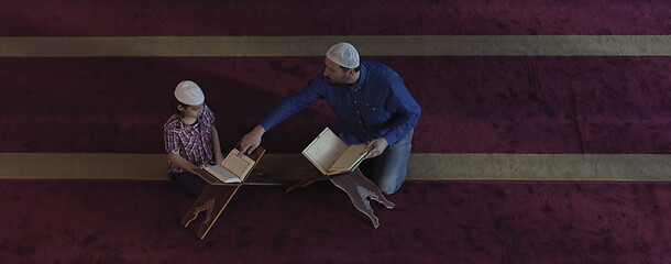 Image showing father and son in mosque praying and reading holly book quran to