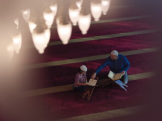 Image showing father and son in mosque praying and reading holly book quran to