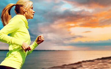 Image showing woman with earphones running over sea sunset