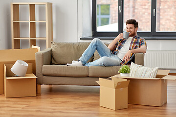 Image showing man with boxes and drinking coffee at new home