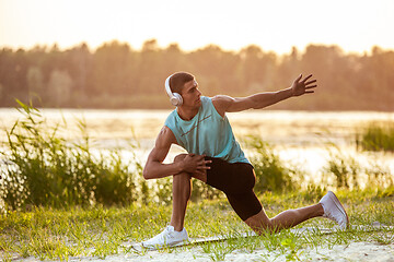 Image showing A young athletic man working out listening to the music at the riverside outdoors