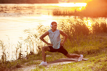 Image showing A young athletic man working out listening to the music at the riverside outdoors