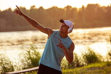 Image showing A young athletic man working out listening to the music at the riverside outdoors