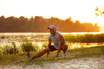 Image showing A young athletic man working out listening to the music at the riverside outdoors