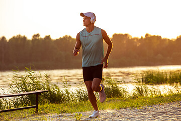 Image showing A young athletic man working out listening to the music at the riverside outdoors