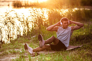 Image showing A young athletic man working out listening to the music at the riverside outdoors