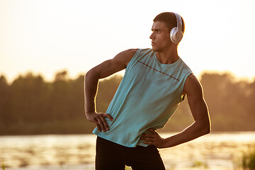 Image showing A young athletic man working out listening to the music at the riverside outdoors