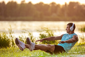 Image showing A young athletic man working out listening to the music at the riverside outdoors