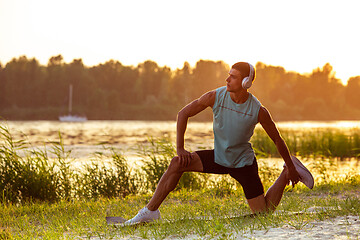 Image showing A young athletic man working out listening to the music at the riverside outdoors