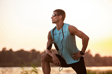 Image showing A young athletic man working out listening to the music at the riverside outdoors