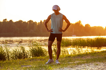 Image showing A young athletic man working out listening to the music at the riverside outdoors