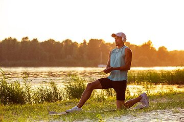 Image showing A young athletic man working out listening to the music at the riverside outdoors