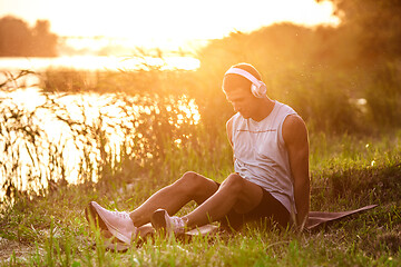 Image showing A young athletic man working out listening to the music at the riverside outdoors