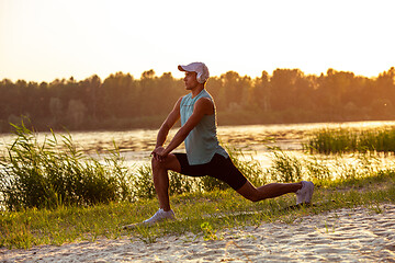 Image showing A young athletic man working out listening to the music at the riverside outdoors