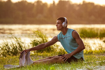 Image showing A young athletic man working out listening to the music at the riverside outdoors