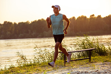 Image showing A young athletic man working out listening to the music at the riverside outdoors