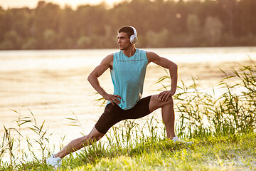 Image showing A young athletic man working out listening to the music at the riverside outdoors