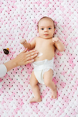 Image showing hand applying body lotion to baby girl\'s tummy