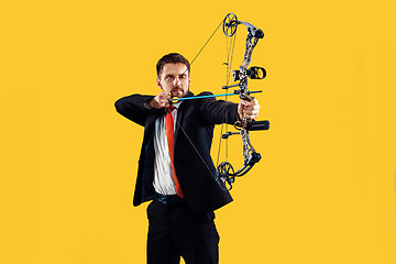 Image showing Businessman aiming at target with bow and arrow, isolated on yellow background