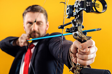 Image showing Businessman aiming at target with bow and arrow, isolated on yellow background