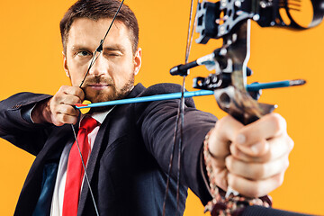 Image showing Businessman aiming at target with bow and arrow, isolated on yellow background