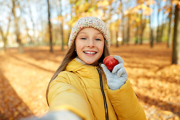 Image showing happy girl with apple taking selfie at autumn park