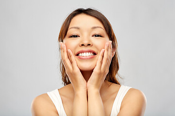 Image showing happy smiling young asian woman touching her face